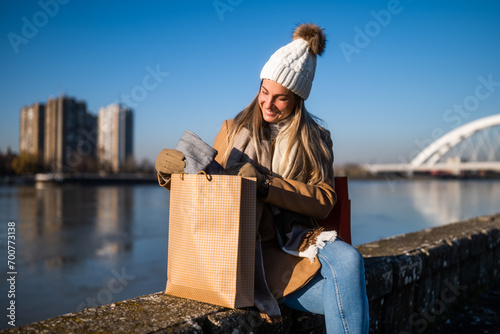 Happy woman in warm clothing with shopping bag enjoys sitting  by river on sunny winter day.  © inesbazdar