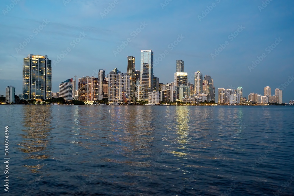 City of Miami, Florida skyline and lights reflected in calm water of Biscayne Bay in clear late evening twilight.