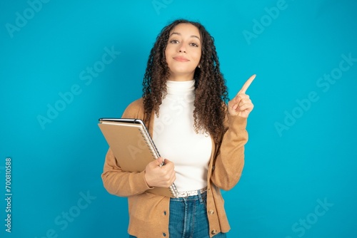 beautiful teen woman wearing beige knitted jacket smiling and looking friendly, showing number one or first with hand forward, counting down
