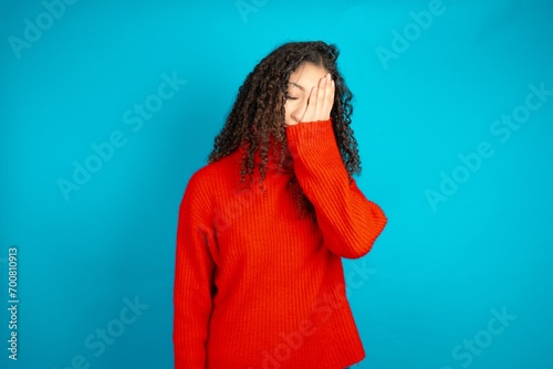 beautiful teen girl wearing red knitted sweater with sad expression covering face with hands while crying. Depression concept.