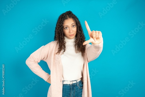 Beautibul teen girl wearing casual clothes making fun of people with fingers on forehead doing loser gesture mocking and insulting.