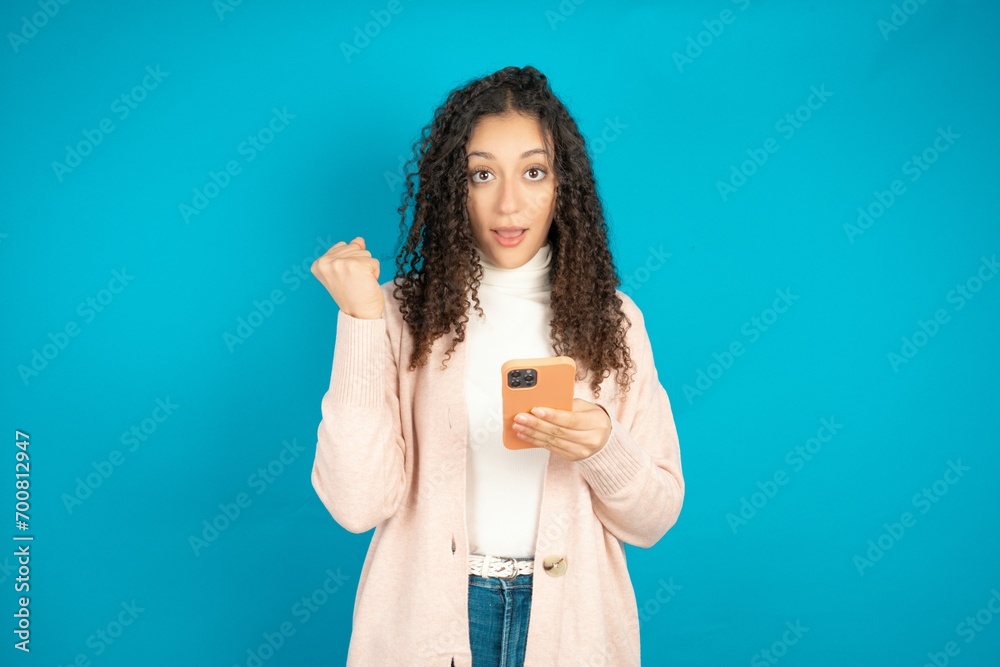 Portrait of Beautibul teen girl wearing casual clothes holding in hands cell celebrating