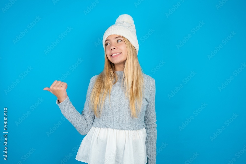 Charming Teen caucasian girl wearing blue knitted sweater and woolly hat looking at copy space having advertisements Charming Teen caucasian girl wearing blue knitted sweater and woolly hat looking at copy space having advertisements