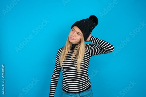 Teen caucasian girl wearing striped sweater and woolly hat confuse and wonder about question. Uncertain with doubt, thinking with hand on head. Pensive concept.
