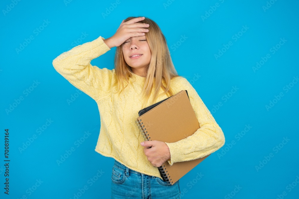 Beautiful kid girl wearing yellow sweater holding notebook Touching forehead for illness and fever, flu and cold, virus sick. Beautiful kid girl wearing yellow sweater holding notebook Touching forehead for illness and fever, flu and cold, virus sick.
