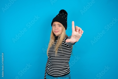 Teen caucasian girl wearing striped sweater and woolly hat making fun of people with fingers on forehead doing loser gesture mocking and insulting. photo