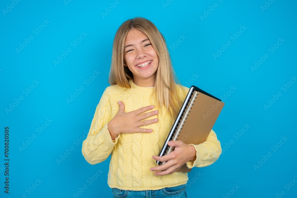 Beautiful kid girl wearing yellow sweater holding notebook smiles toothily cannot believe eyes expresses good emotions and surprisement Beautiful kid girl wearing yellow sweater holding notebook smiles toothily cannot believe eyes expresses good emotions and surprisement