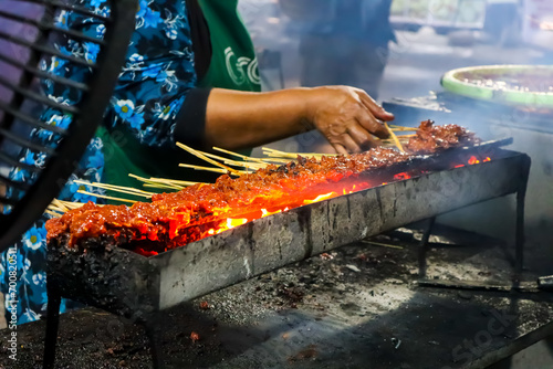 Hand of indonesian woman preparing satay in traditional charcoal satay grill photo
