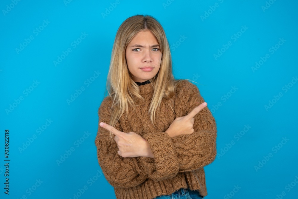 Serious beautiful caucasian teen girl wearing yellow sweater crosses hands and points at different sides hesitates between two items. Hard decision concept Serious beautiful caucasian teen girl wearing yellow sweater crosses hands and points at different sides hesitates between two items. Hard decision concept