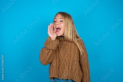 beautiful caucasian teen girl wearing brown sweater look empty space holding hand face and screaming or calling someone.