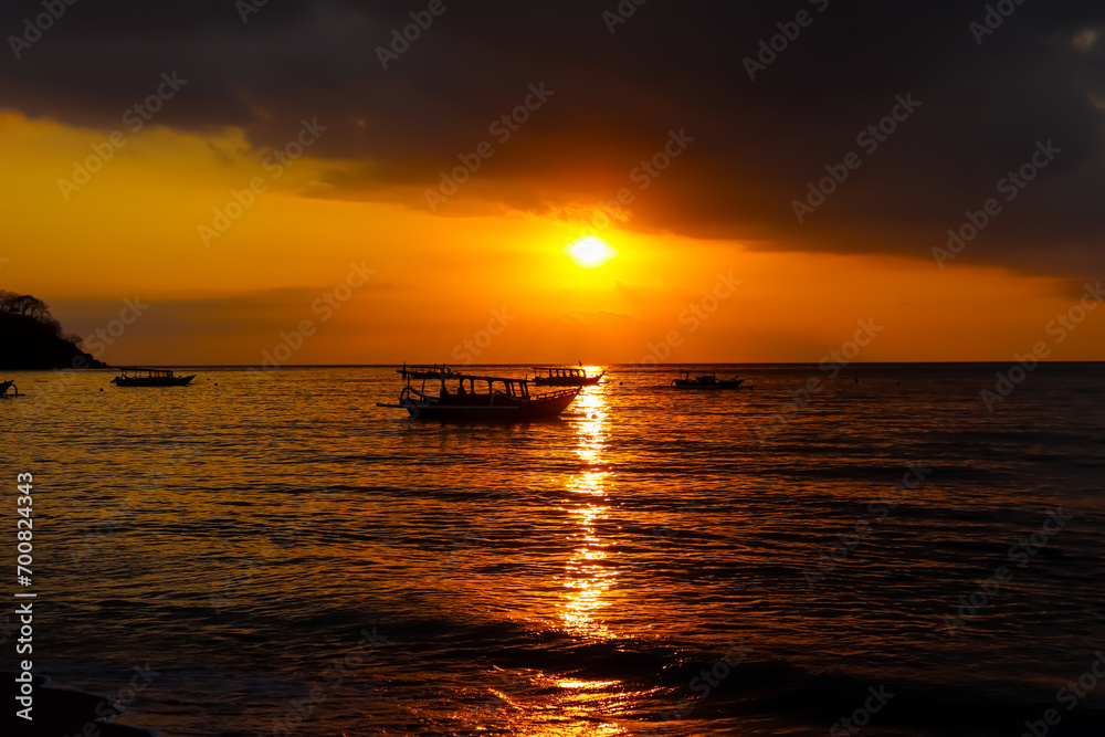 Scenic view of dramatic sunset in the beach with silhouette boats on the sea