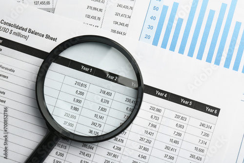 Magnifying glass on accounting documents with data and graph  top view