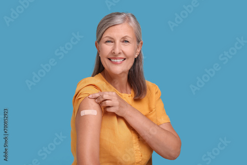 Senior woman with adhesive bandage on her arm after vaccination against light blue background
