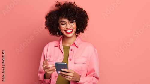 Very happy woman with long hair checking her phone and smiling on a pink clean background 