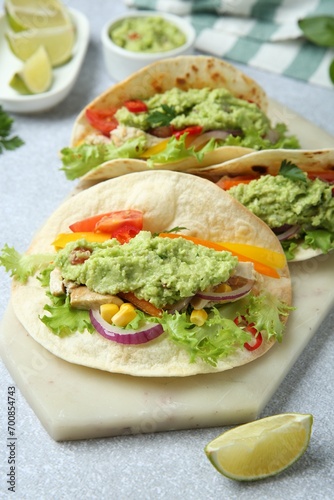 Delicious tacos with guacamole, meat and vegetables on light grey table