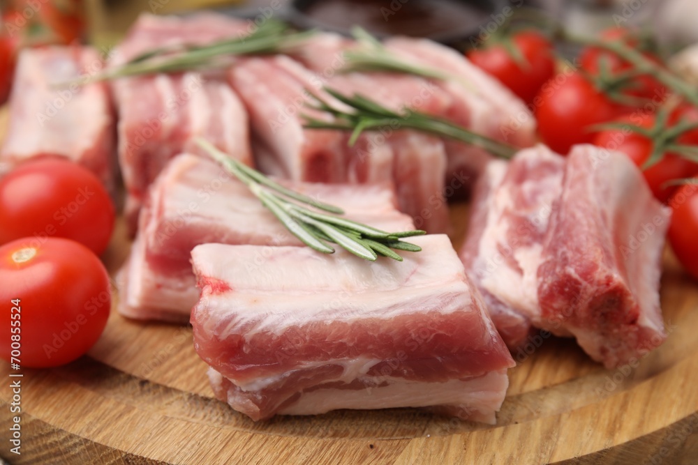 Cut raw pork ribs with rosemary and tomatoes on wooden board, closeup