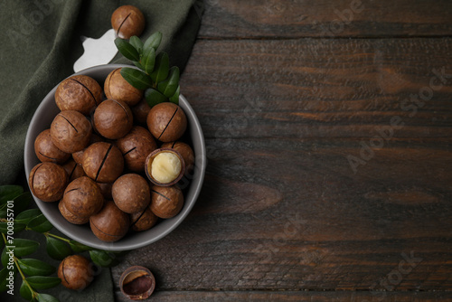 Tasty Macadamia nuts in bowl and green twigs on wooden table, flat lay. Space for text