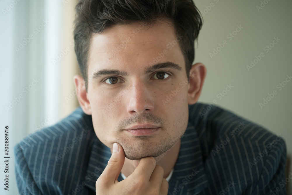 Close-up of young handsome guy in a white shirt, looks seriously and intently at the camera indoor