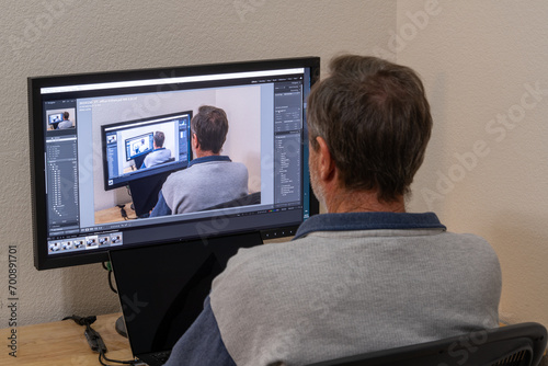 Mature Caucasian man sitting at a desk of a home office working on a picture within picture on a computer screen with photo management, editing software