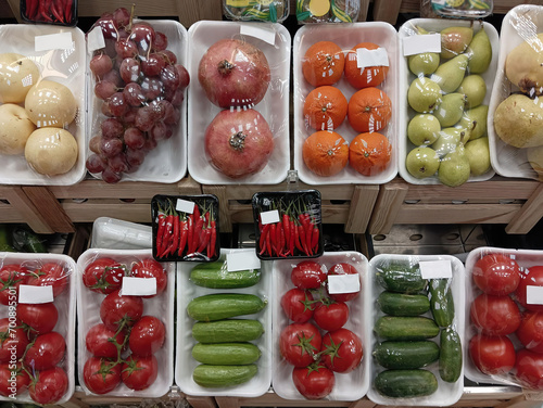 Group of fresh vegetables and fruits packed with stretch on supermarket counter of groceries. tomatoes in plastic container.  transparent foil