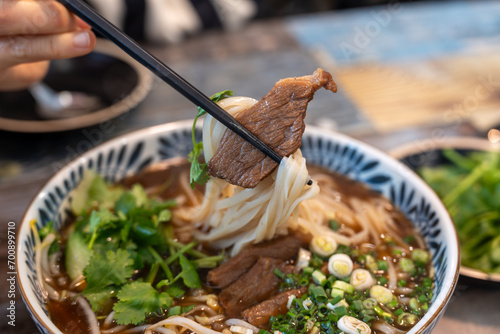 Closeup photo of beef rice noodle (pho) held in chopsticks, taken in a restaurant photo