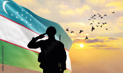 Silhouette of a soldier with the Uzbekistan flag stands against the background of a sunset or sunrise. Concept of national holidays. Commemoration Day. photo