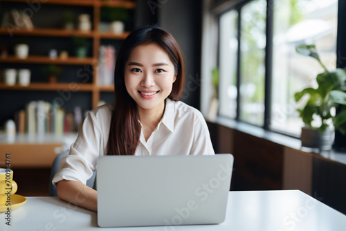 Young Asian woman sitting at desk with laptop in home office