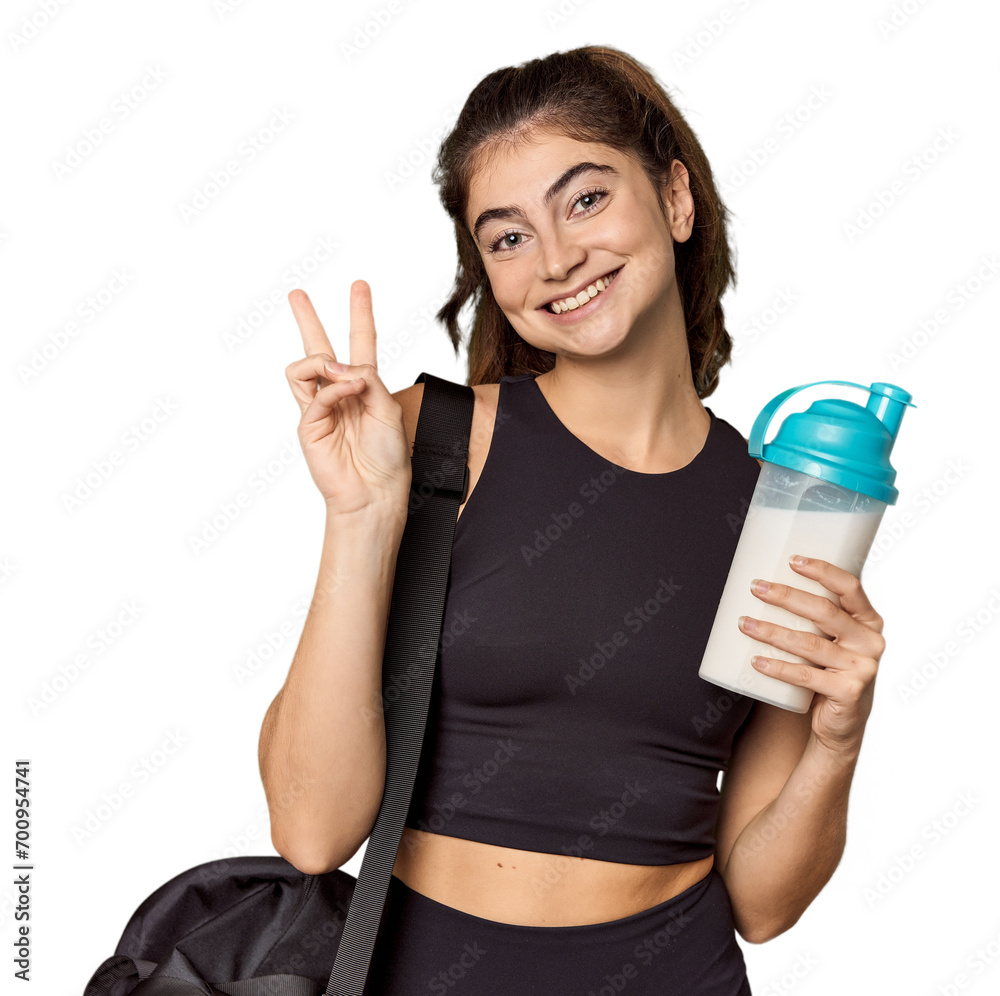Athletic Caucasian woman holding protein shake joyful and carefree showing a peace symbol with fingers. Athletic Caucasian woman holding protein shake joyful and carefree showing a peace symbol with fingers.