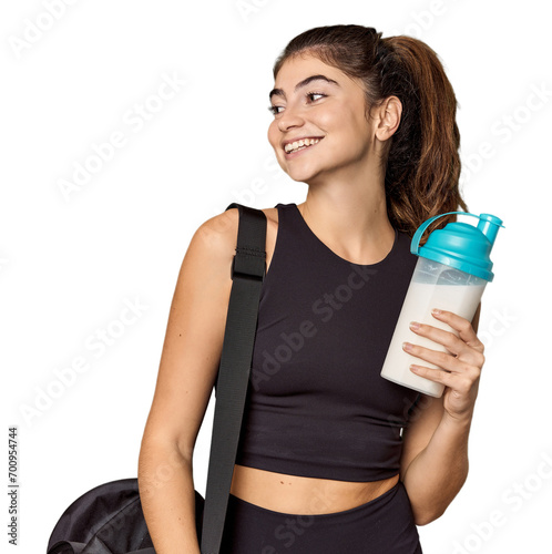 Athletic Caucasian woman holding protein shake looks aside smiling, cheerful and pleasant.