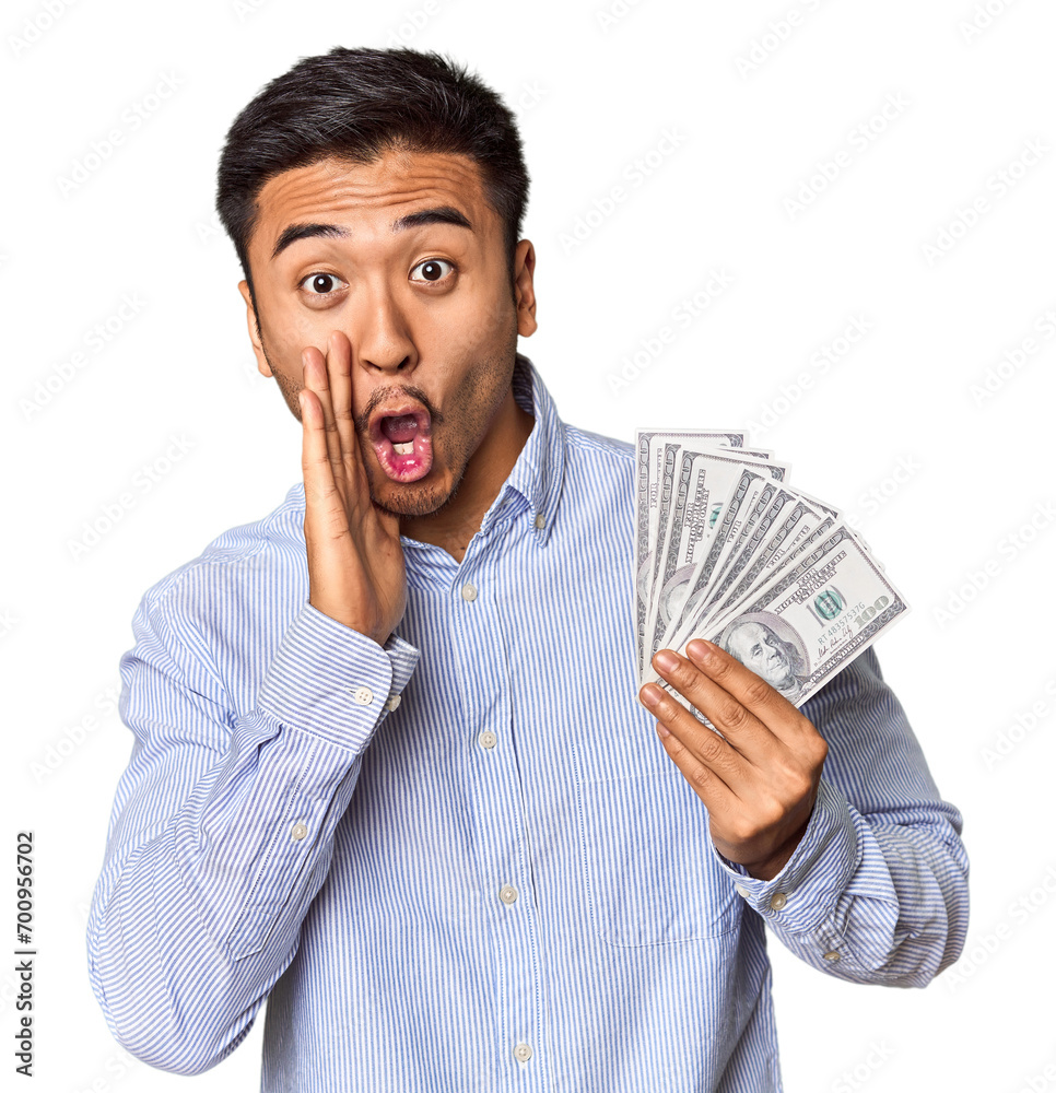Young Chinese man holding dollar bills in studio is saying a secret hot braking news and looking aside Young Chinese man holding dollar bills in studio is saying a secret hot braking news and looking aside