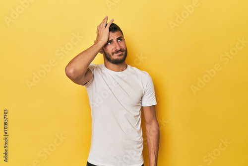 Young Hispanic man on yellow background forgetting something, slapping forehead with palm and closing eyes. photo