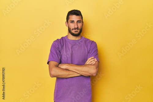 Young Hispanic man on yellow background who feels confident, crossing arms with determination.