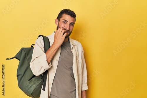 Young Hispanic man with travel backpack biting fingernails, nervous and very anxious.