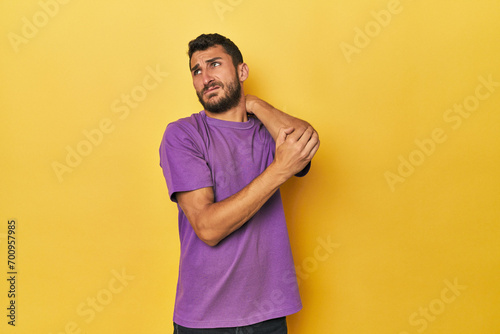 Young Hispanic man on yellow background massaging elbow, suffering after a bad movement.