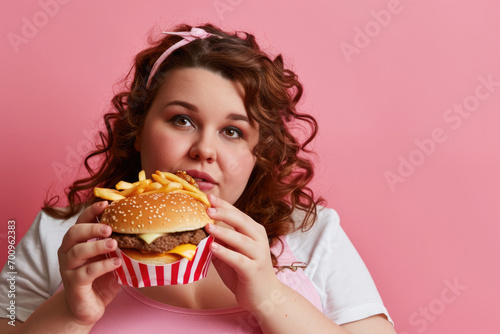 Very fat girl eating a hamburger on a coloured background, fast food is bad for health