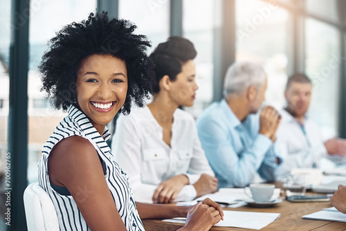 Shes an invaluable member of the team. Portrait of a smiling businesswoman sitting in a boardroom with colleagues in the background. photo