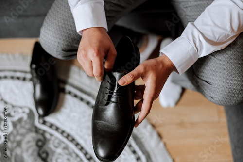 An elegant man wears black leather formal shoes. Tying shoes. Business man tying shoelaces on the floor. Up close The groom is preparing for the wedding. photo