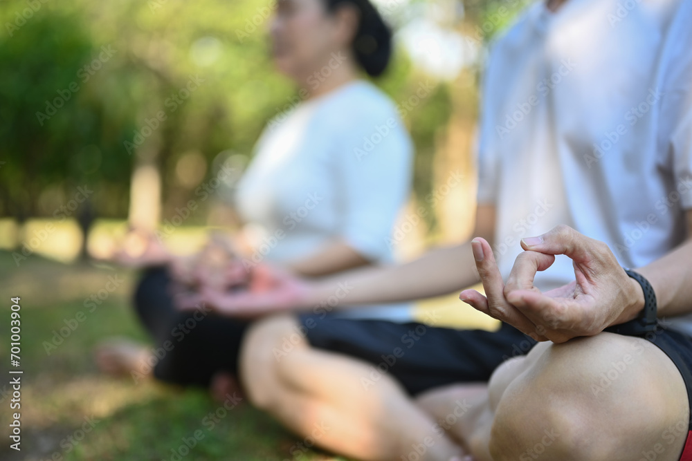 Close up shot of senior couple meditating sitting in lotus pose at summer park. Healthy lifestyle concept.
