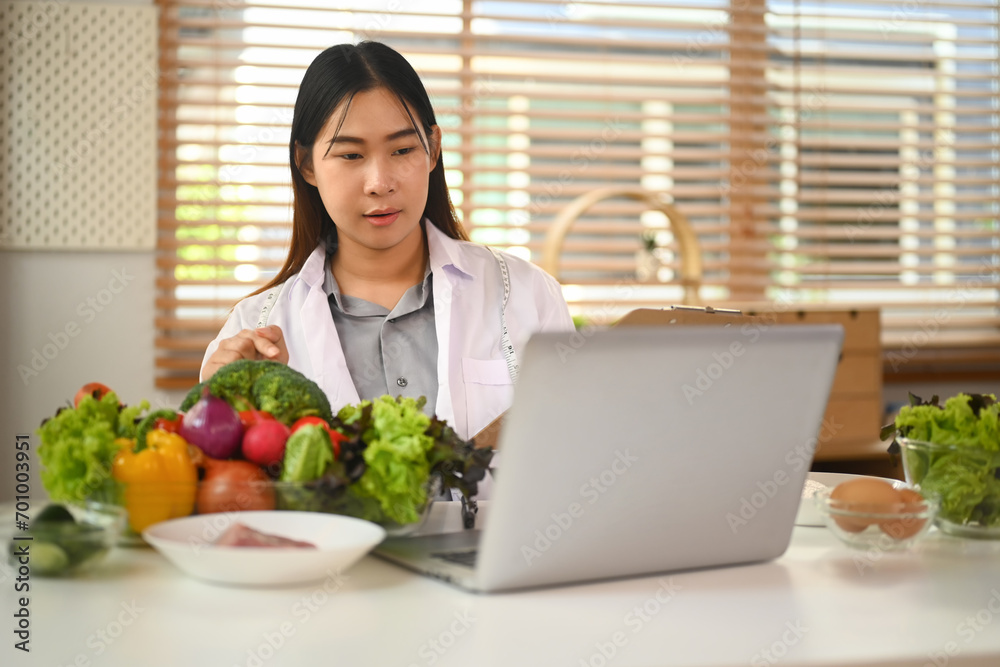 Female nutritionist in white coat calling patient and giving online consultation on laptop computer Female nutritionist in white coat calling patient and giving online consultation on laptop computer