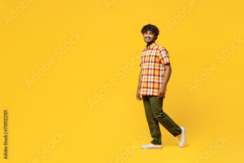Full body side view smiling happy cheerful fun young Indian man he wears shirt casual clothes walking going looking camera isolated on plain yellow color background studio portrait. Lifestyle concept.
