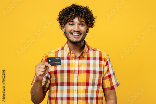 Young smiling happy cheerful satisfied Indian man he wears shirt casual clothes hold in hand mock up of credit bank card isolated on plain yellow color background studio portrait. Lifestyle concept.