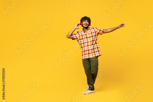 Full body young cheerful fun happy cool Indian man he wearing shirt casual clothes dancing listen to music in headphones isolated on plain yellow color background studio portrait. Lifestyle concept. photo