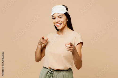 Young calm Latin woman wear pyjamas jam sleep eye mask rest relax at home point index finger camera on you encourage isolated on plain pastel light beige background studio Good mood night nap concept