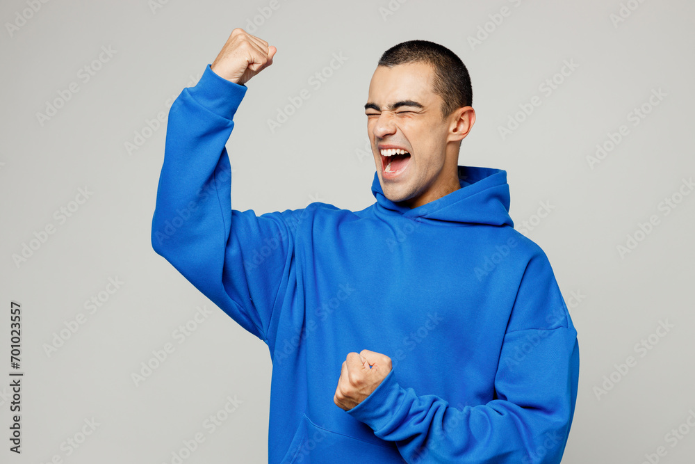 Young happy excited fun middle eastern man he wear blue hoody casual clothes doing winner gesture celebrate clenching fists isolated on plain solid white background studio portrait. Lifestyle concept. Young happy excited fun middle eastern man he wear blue hoody casual clothes doing winner gesture celebrate clenching fists isolated on plain solid white background studio portrait. Lifestyle concept.