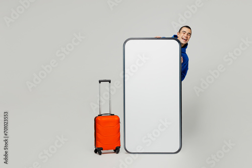 Traveler young man wear hold bag big huge blank screen mobile cell phone isolated on plain solid white background Tourist travel abroad in free spare time rest getaway Air flight trip journey concept #701023553