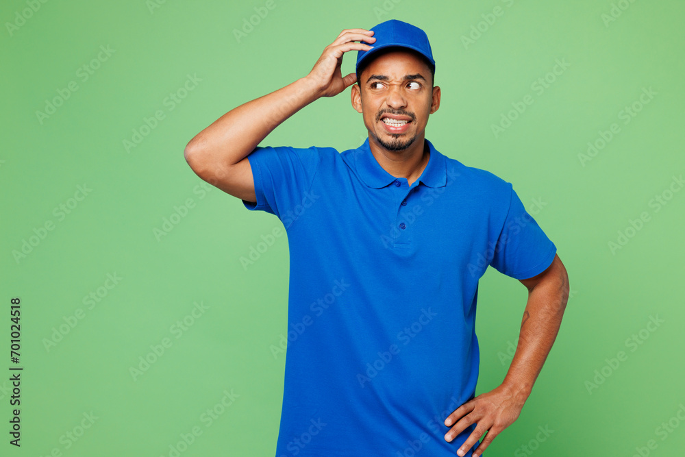 Professional mistaken confused delivery guy employee man wear blue cap t-shirt uniform workwear work as dealer courier look aside hold scratch head isolated on plain green background. Service concept.