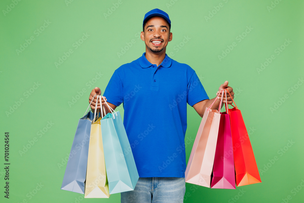 Delivery guy employee man wears blue cap t-shirt uniform workwear work as dealer courier hold package bags after shopping isolated on plain green background. Service, Black Friday sale buy day concept Delivery guy employee man wears blue cap t-shirt uniform workwear work as dealer courier hold package bags after shopping isolated on plain green background. Service, Black Friday sale buy day concept