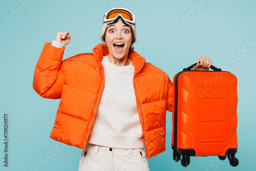 Traveler happy skier woman wear padded windbreaker jacket ski goggles mask hold suitcase bag isolated on plain blue background. Tourist travel abroad in free time rest getaway Air flight trip concept #701024977