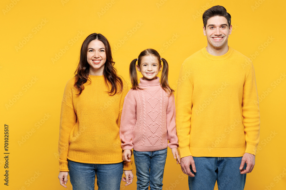 Young smiling cool fun happy positive parents mom dad with child kid girl 7-8 years old wearing pink knitted sweater casual clothes look camera isolated on plain yellow background. Family day concept.