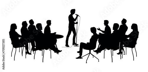 Man stand up comedian performs on stage in front of audience silhouettes.